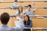 Students sitting at the lecture hall with man raising hand to ask question