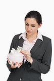 Brunette in suit putting dollars into a piggy-bank