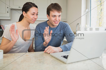Couple using laptop for video chat and waving