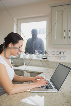 Woman using laptop with robber looking at her through window