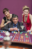 Women standing with man at roulette table