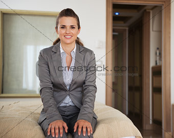 Happy business woman sitting on bed in hotel room
