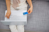 Closeup on credit card in hand of young woman sitting on couch