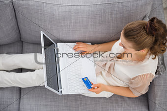 Young woman laying on sofa with laptop and credit card
