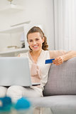 Smiling young housewife with laptop and credit card in living ro