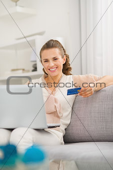 Smiling young housewife with laptop and credit card in living ro