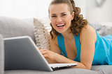 Smiling young woman laying on sofa with laptop