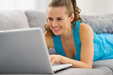 Smiling young woman laying on couch with laptop