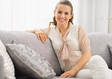 Portrait of smiling young housewife sitting on couch in living r