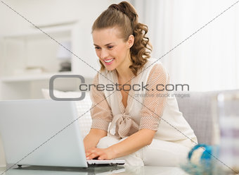 Happy young housewife using laptop in living room