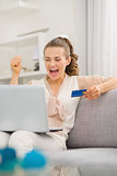 Happy young housewife with laptop and credit card rejoicing succ