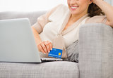 Closeup on credit card in hand of smiling woman with laptop
