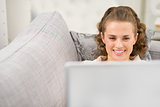 Happy young woman laying on divan with laptop