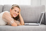 Thoughtful young woman laying on sofa with laptop