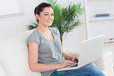 Smiling woman sitting on a couch and using a laptop