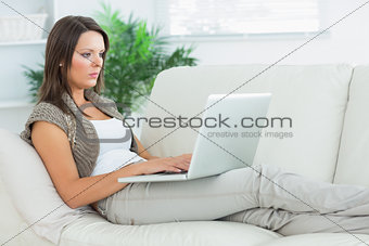 Serious woman lying on the sofa and using her laptop