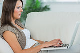 Thoughtful woman lying on the sofa and using her laptop