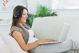 Happy woman listening music with her laptop and lying on sofa
