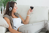 Woman lying on the sofa and listening to music with a red wine glass