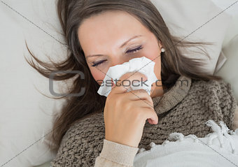 Sick woman lying on sofa and blowing nose