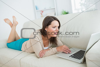Brunette lying on sofa and using her laptop