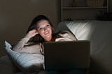 Woman lying on sofa with her laptop in night