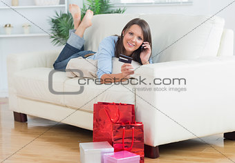 Woman lying on sofa holding a credit card and calling