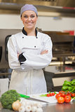 Smiling chef folding her arms beside vegetables