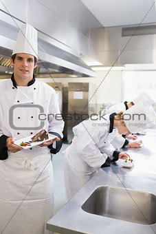 Chef presenting desert with others working on deserts