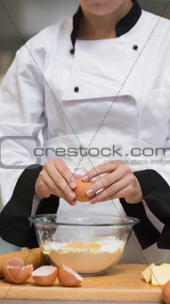 Chef cracking egg into bowl of flour