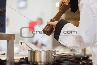Chef adding pepper to soup