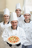 Chef presenting pizza with others behind him