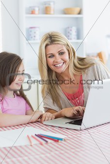 Mother and girl sitting at the kitchen with laptop