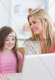 Mother smiling at daughter using laptop