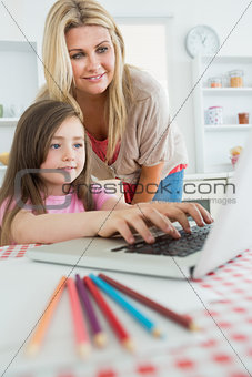 Woman standing looking at Daughter typing