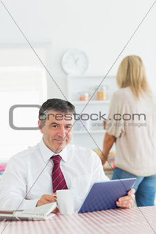 Smiling man with tablet pc and coffee at kitchen table