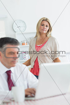 Wife looking upset at husband using laptop in kitchen