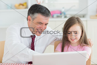 Man and girl sitting at the kitchen with laptop