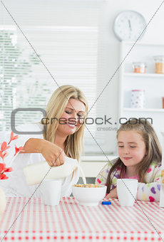 Mother pouring milk into cereal bowl for daughter