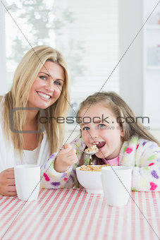 Little girl eating cereal at breakfast with her mother