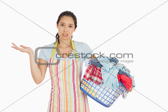 Puzzled young woman holding laundry basket full of dirty laundry