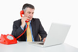 Serious man phoning while writing on laptop