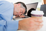 Man sleeping on his laptop while holding coffee