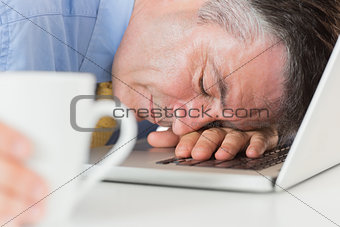 Businessman sleeping on his laptop while holding coffee