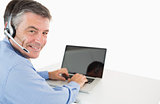 Smiling businessman with headset working on laptop