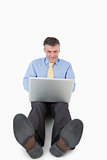 Smiling man writing on his laptop on the floor