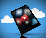 Tablet pc showing play button standing against background with clouds