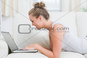 Cheerful woman using laptop while lying