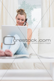 Woman lying on the couch while using mobile phone and laptop