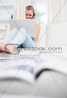 Woman sitting on the couch while using laptop and calling